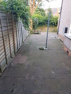 an empty sidewalk next to a wooden fence and tree in the back yard with no leaves on it