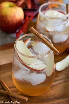 two glasses filled with apple cider on top of a cutting board