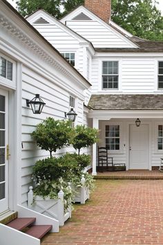 a white house with brick walkway and potted plants on the front door step area