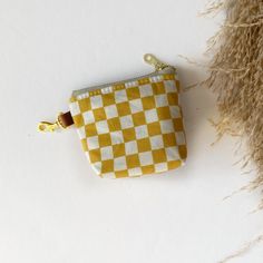 a small yellow and white checkered purse sitting on top of a table next to dried grass