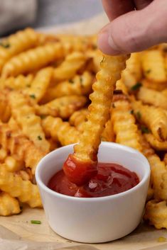 a person dipping ketchup into some cheesy fries