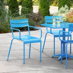 a blue table and chairs sitting on top of a cement floor next to bushes with flowers in the background