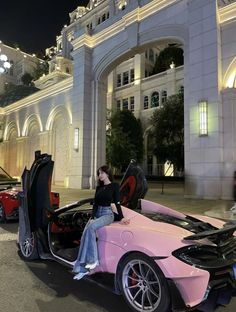 a woman sitting on the hood of a pink sports car in front of a building