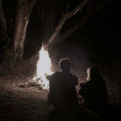 two people sitting around a fire in the dark with their backs turned to the camera