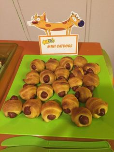 a green table topped with lots of hotdogs and croissants on top of it