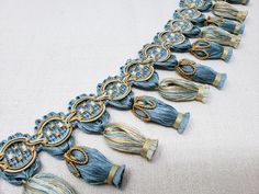 a blue and gold necklace with tassels on it's sides is laying on a white surface