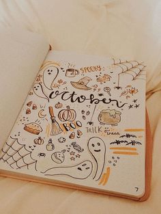 an open notebook with halloween doodles on the cover sitting on top of a bed