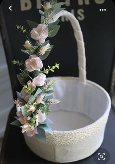 a white basket with flowers and greenery in it sitting on a table next to a black chair