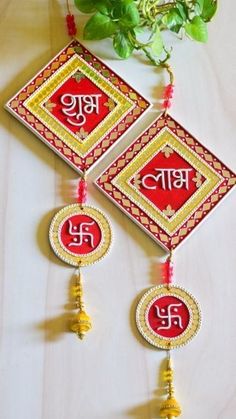 two red and gold ornaments hanging from a wall next to a potted green plant