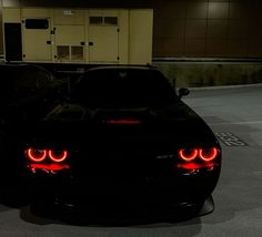 the back end of a black sports car with its lights turned on at night time