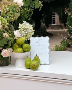 some pears are in a bowl on a table near flowers and a sign that says love