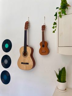 two ukulele guitars are hanging on the wall next to plants and record discs