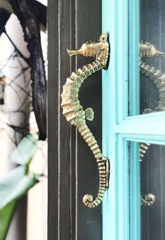 a close up of a door with a sea horse on it's side and a plant in the background