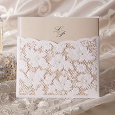 a wedding card with white lace and flowers on it, sitting next to a bouquet of daisies