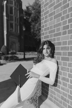 a woman leaning against a brick wall holding a book