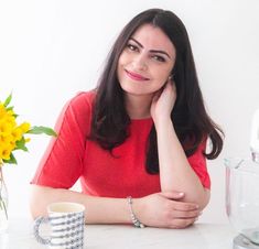 a woman sitting at a table next to a vase with sunflowers