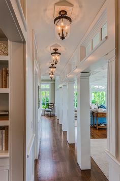 a long hallway with white walls and wood flooring is lit by chandeliers