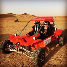 a man driving an orange dune buggy in the middle of the desert with two people inside