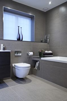 a white toilet sitting next to a bath tub in a bathroom under a large window