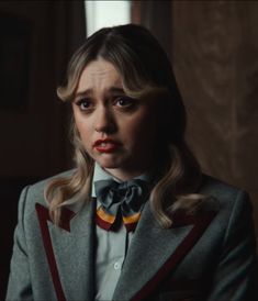 a woman with blonde hair wearing a grey suit and bow tie in a dark room