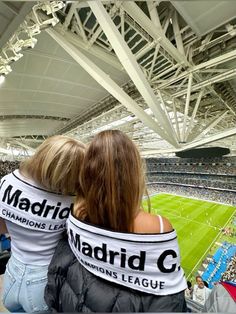 two women are sitting in the stands at a soccer game, one is wearing a scarf