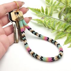 a hand holding a keychain that is decorated with multicolored seed beads