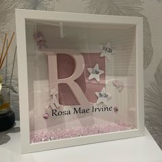 the letter r is made out of paper and surrounded by pink confetti in a white frame