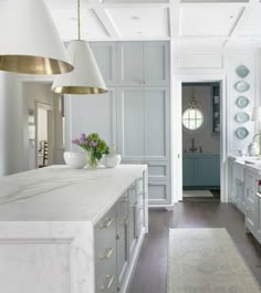 a large kitchen with marble counter tops and white cabinets, along with two pendant lights hanging from the ceiling