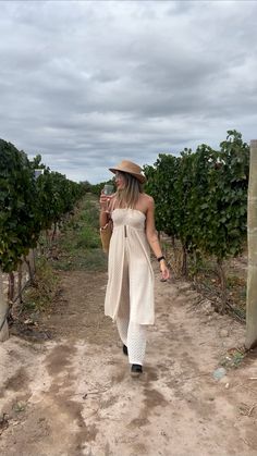 a woman walking down a dirt road with a hat on