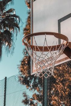 a basketball hoop hanging from the side of a fence with trees in the back ground