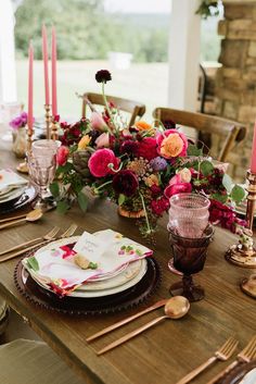 the table is set with pink and red flowers, gold place settings, and candles