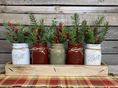 four mason jars with pine branches and berries in them