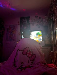 a person with a hello kitty blanket on sitting in front of a television screen and looking into the room