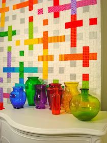 colorful vases are lined up on a white table in front of a mosaic wall