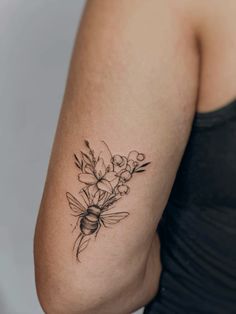 a woman's arm with flowers and a bee tattoo on the back of her shoulder