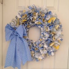 a wreath with blue and yellow flowers hanging on the front door, next to a bow