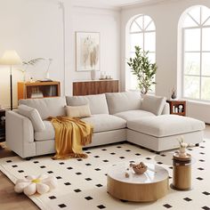 a living room with a large sectional couch and coffee table in front of two windows