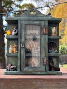 an old green cabinet with shells and other items in it sitting on a wooden table