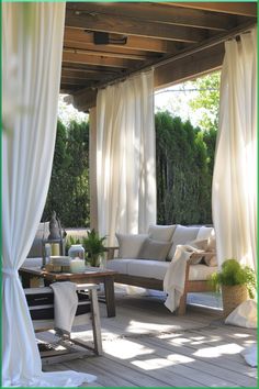 an outdoor living area with white curtains and furniture