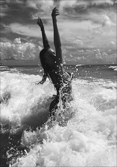 a woman is in the water with her arms up as she rides on a surfboard