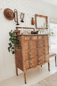 an old dresser with lots of drawers in the corner next to a mirror and potted plant