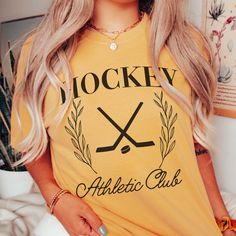 Gear up your inventory with our Hockey Athletic Club Comfort Color Tee, a must-have for fans of the game looking to showcase their passion in style. Crafted with premium materials and featuring a dynamic design, this tee is the perfect addition to any sports enthusiast's wardrobe. For those who bleed hockey, this tee is a statement piece, boasting bold graphics and vibrant colors that capture the essence of the game. Whether you're cheering from the stands or hitting the ice yourself, this tee i Collegiate T-shirt With Sublimation Print For Sports Events, Sporty College T-shirt With Team Logo, Athleisure Tops With Sublimation Print For Sports Events, Sporty Team Logo Top For Sports Season, Sporty Fan Merchandise Tops With Team Logo, Sporty Tops With Team Logo For Sports Events, Sporty Top With Team Logo For Sports Season, Sporty T-shirt For Game Day, Sporty Tops For Sports Season Fan Merchandise