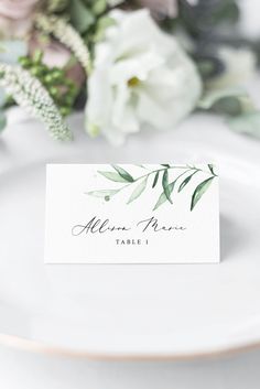 a place card on a plate with flowers and greenery in the background for an elegant table setting