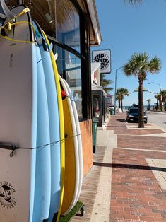 several surfboards leaning up against the side of a building on a sidewalk near palm trees