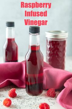 raspberry infused vinegar in two glass bottles on a table with raspberries