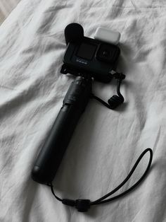 a camera attached to a microphone laying on top of a white bed sheet with a black cord