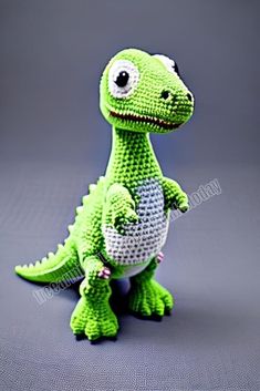 a small green toy dinosaur sitting on top of a gray surface with its eyes wide open