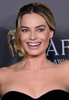 a woman in a strapless black dress smiles at the camera while standing on a red carpet