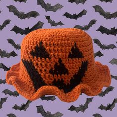 an orange crocheted hat with black bats on it in front of a purple background