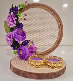 purple flowers and two gold wedding rings on a wooden stand next to an oval mirror